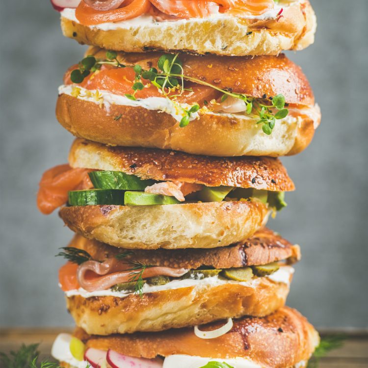 Heap of Bagels with salmon, eggs, vegetables, capers, fresh herbs and cream-cheese, grey concrete background. Healthy breakfast, lunch or take-away food concept