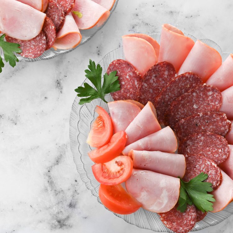 plate with an assortment of boiled, smoked sausage on bright table. Cold cuts of sausage with herbs and vegetables